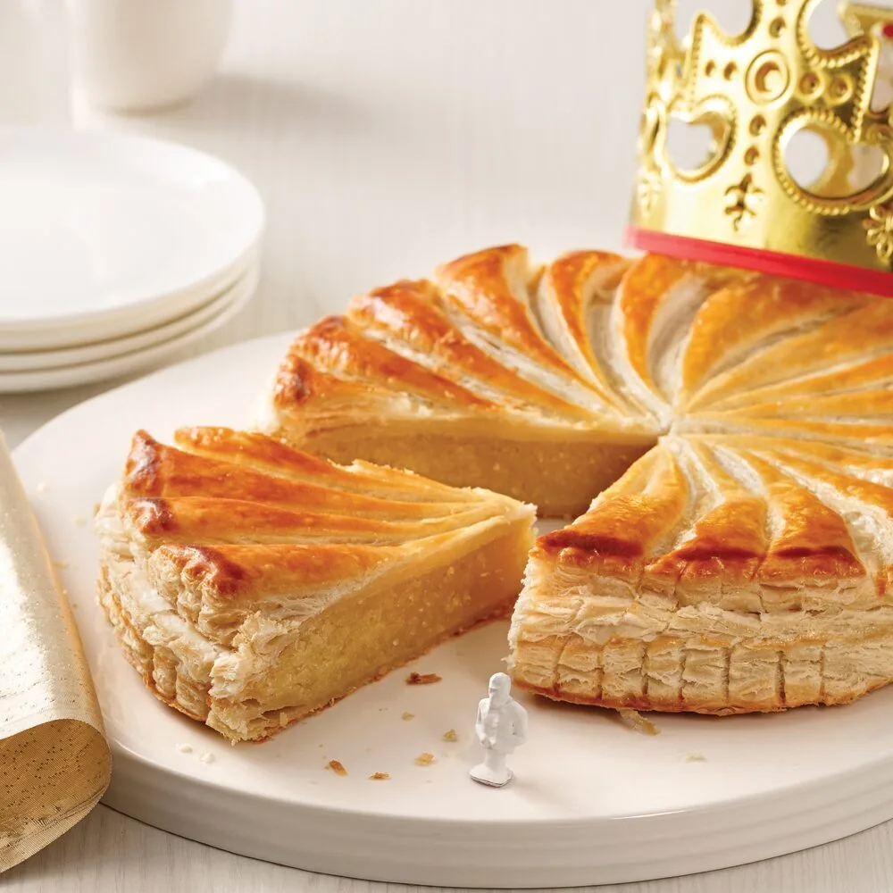 Galette des rois dorée entamée, couronne et fève posées sur la table